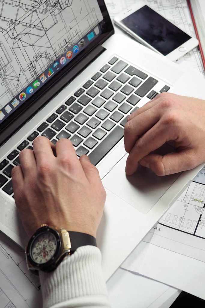 Man Using Turned-on Macbook Pro on White Printer Papers
